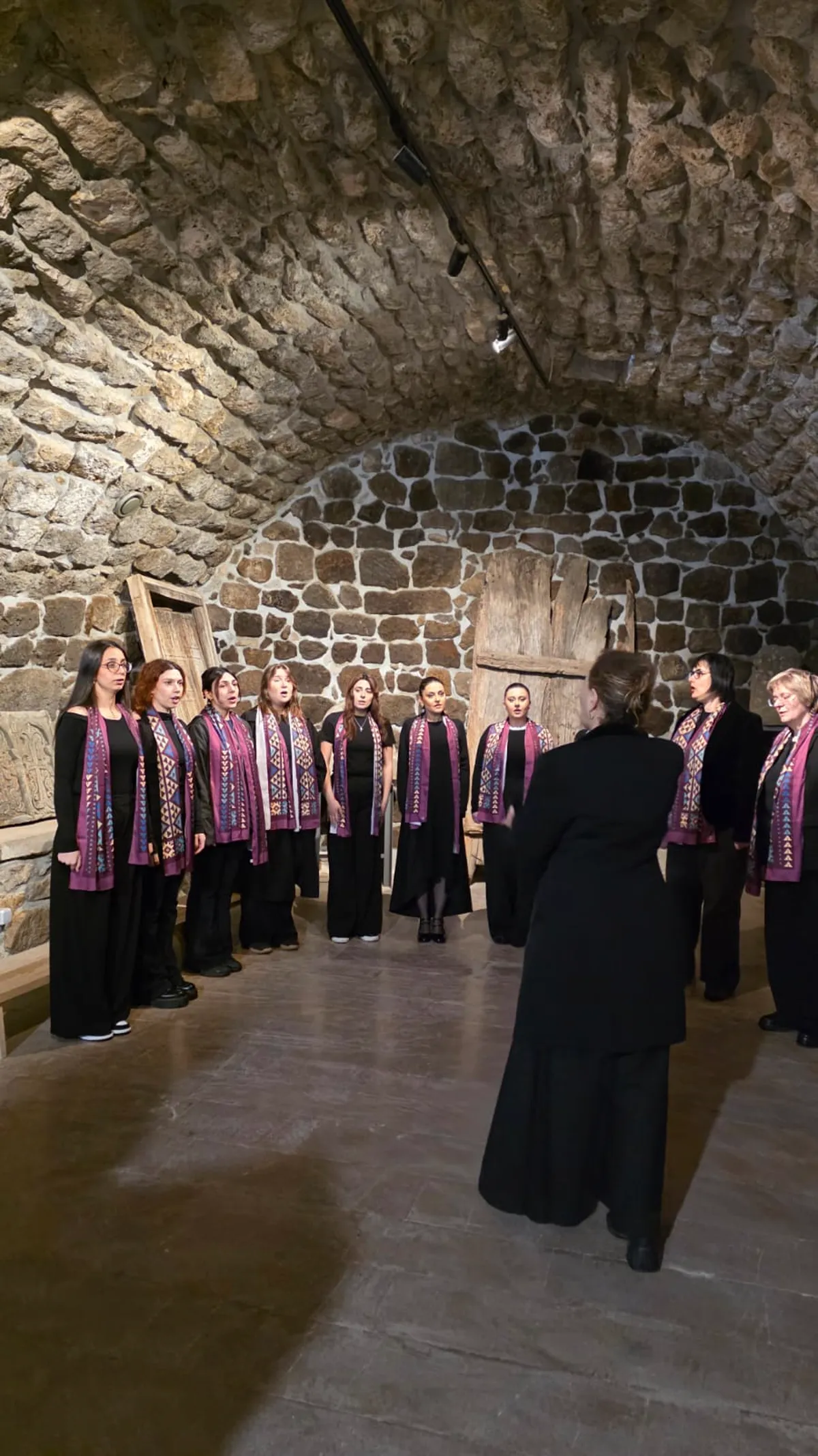 The choir performing in a vaulted stone hall with the conductor in the foreground